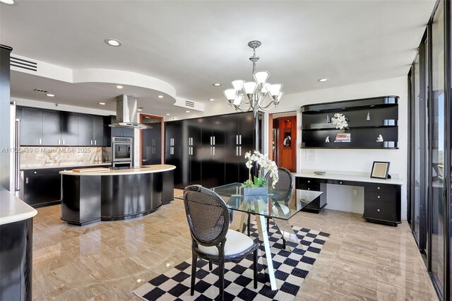 kitchen featuring decorative light fixtures, an island with sink, tasteful backsplash, a notable chandelier, and extractor fan