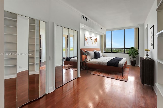 bedroom with dark hardwood / wood-style flooring, two closets, and ornamental molding