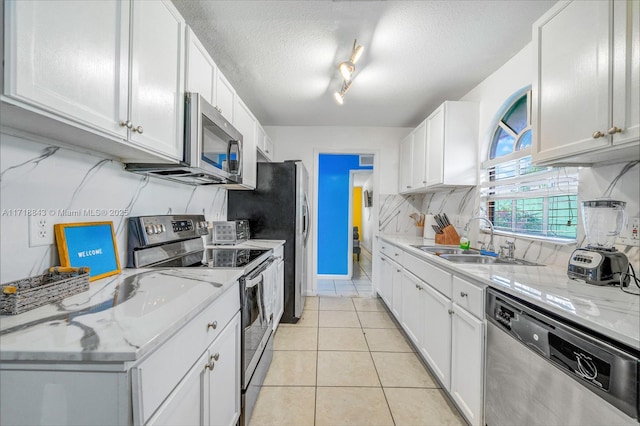 kitchen with white cabinetry, sink, light stone countertops, light tile patterned floors, and appliances with stainless steel finishes