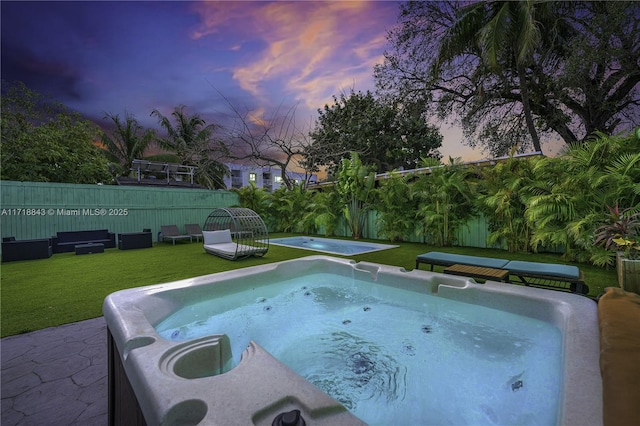 pool at dusk with a lawn and a hot tub