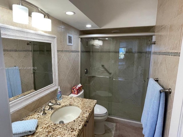 bathroom featuring vanity, toilet, walk in shower, and tile walls