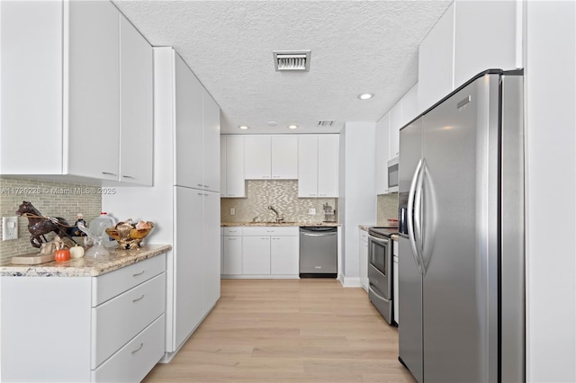 kitchen with backsplash, light hardwood / wood-style flooring, a textured ceiling, appliances with stainless steel finishes, and white cabinetry