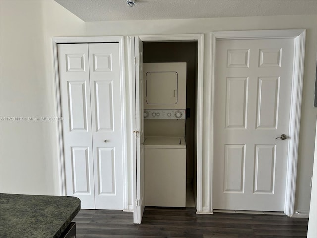 clothes washing area with stacked washer and dryer, a textured ceiling, and dark wood-type flooring