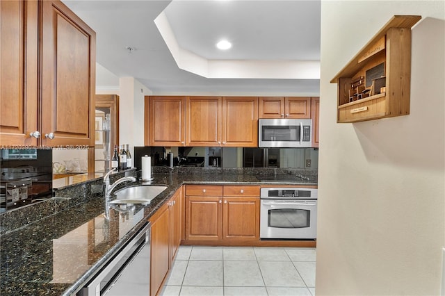 kitchen with dark stone counters, sink, light tile patterned floors, appliances with stainless steel finishes, and a tray ceiling