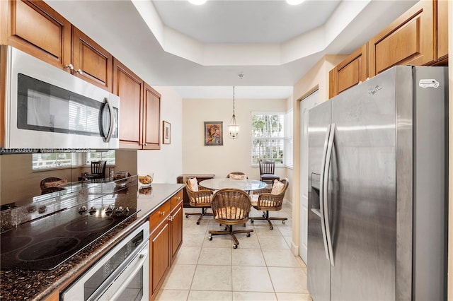 kitchen with pendant lighting, stainless steel appliances, light tile patterned floors, and a tray ceiling