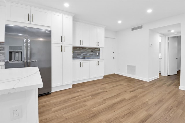 kitchen featuring backsplash, stainless steel refrigerator with ice dispenser, light wood-type flooring, light stone counters, and white cabinetry