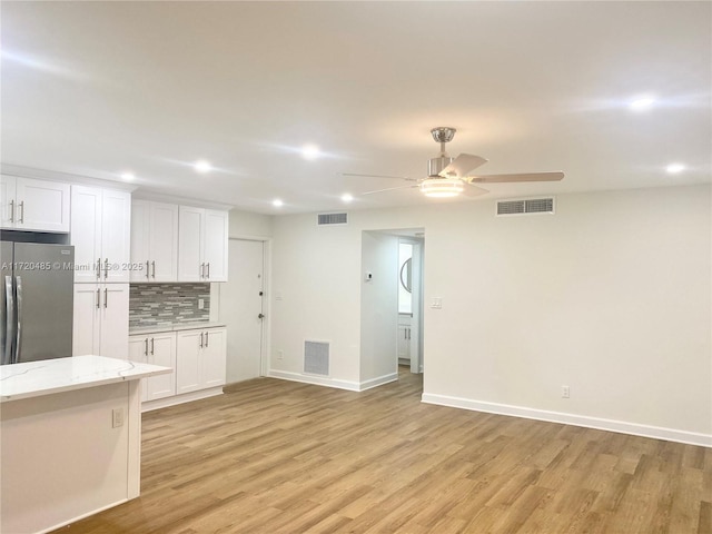 kitchen with backsplash, white cabinets, ceiling fan, stainless steel fridge, and light stone countertops