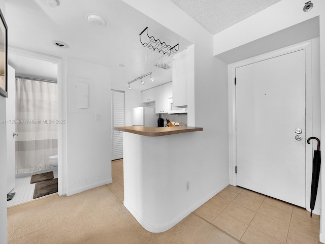 kitchen featuring light tile patterned floors, baseboards, freestanding refrigerator, and white cabinets