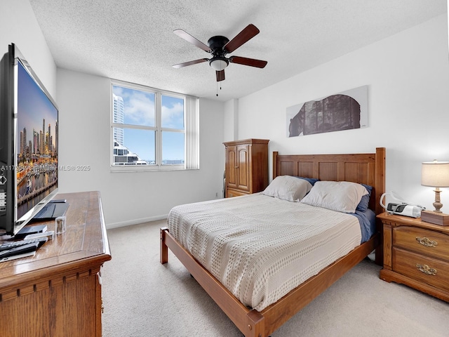 bedroom featuring light colored carpet, ceiling fan, a textured ceiling, and baseboards