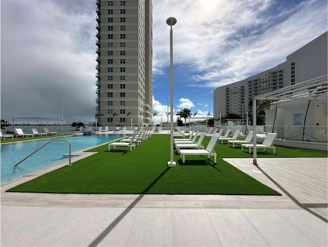 view of community with a view of city, a yard, a swimming pool, and fence