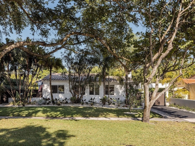 view of front of house with stucco siding, driveway, a tile roof, and a front lawn