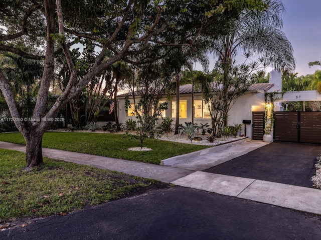 view of front facade with a gate, aphalt driveway, a front lawn, and stucco siding