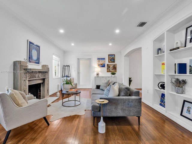 living room featuring visible vents, built in shelves, a fireplace, wood finished floors, and arched walkways