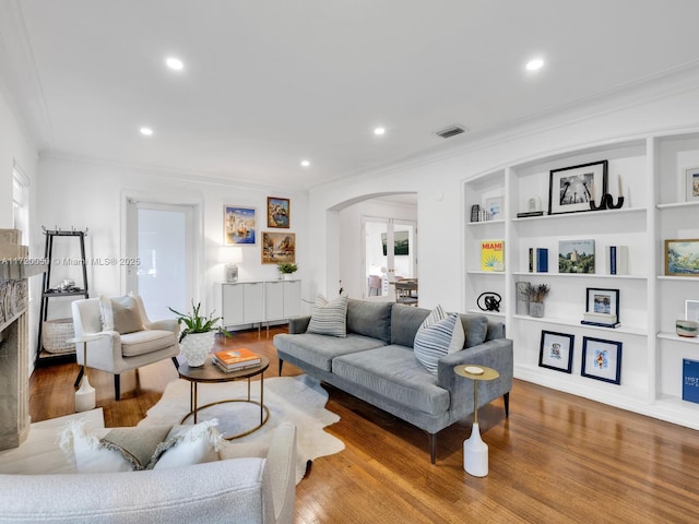 living room with visible vents, arched walkways, wood finished floors, and crown molding