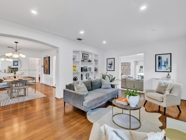 living room featuring built in shelves, visible vents, light wood-style flooring, arched walkways, and crown molding