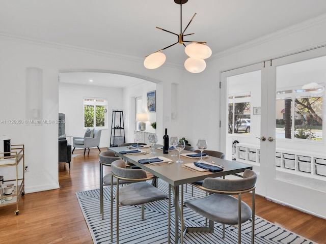 dining space featuring french doors, arched walkways, wood finished floors, and ornamental molding