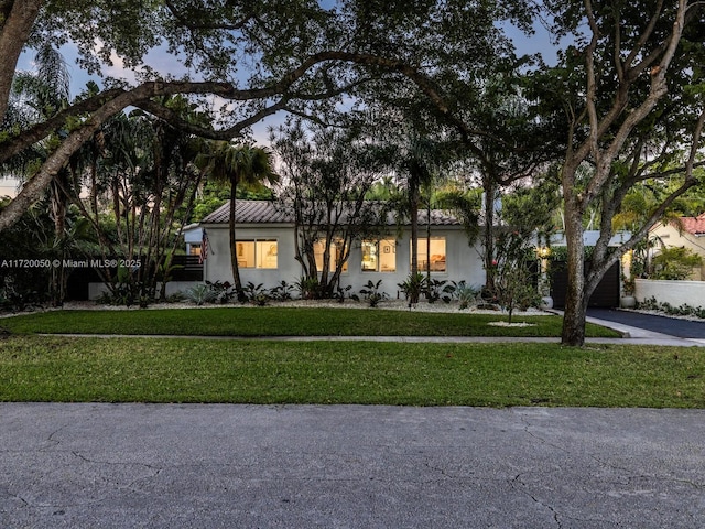 view of front of house featuring a front yard, a tiled roof, driveway, and stucco siding