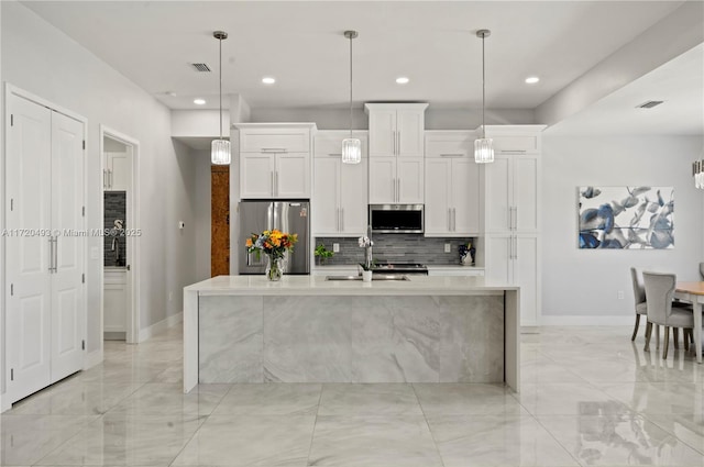 kitchen with white cabinets, appliances with stainless steel finishes, a kitchen island with sink, and pendant lighting