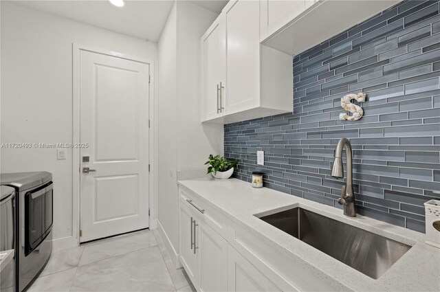 kitchen with sink, tasteful backsplash, light stone counters, washer and clothes dryer, and white cabinets