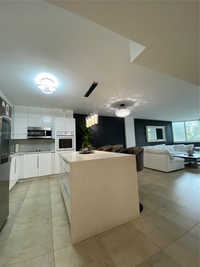 kitchen featuring a center island, white cabinetry, decorative light fixtures, white oven, and backsplash