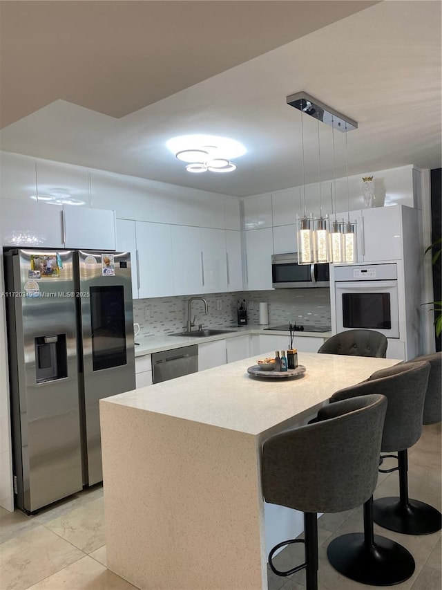 kitchen featuring a center island, decorative light fixtures, white cabinetry, stainless steel appliances, and sink