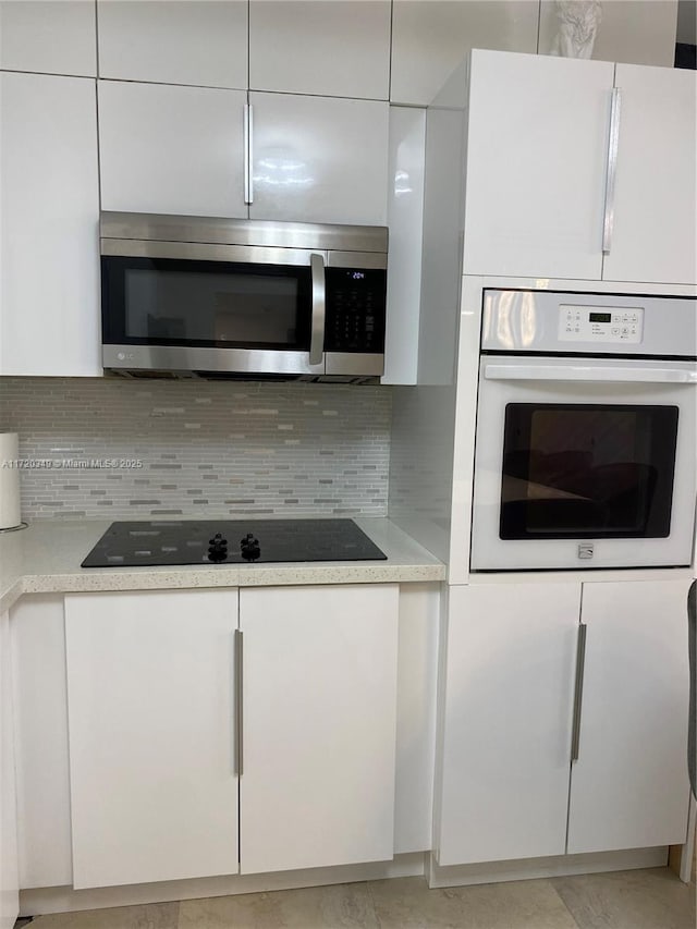 kitchen with black electric cooktop, decorative backsplash, white oven, and white cabinetry