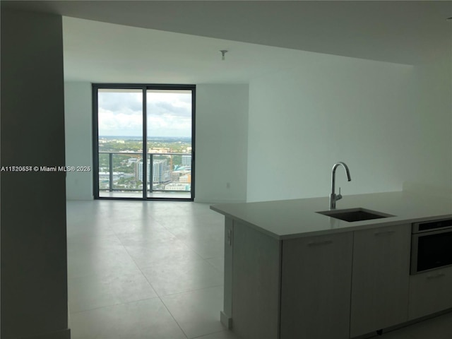 kitchen featuring sink, oven, light tile patterned floors, and a wall of windows