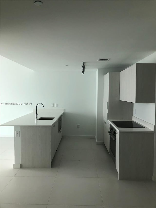 kitchen with black electric stovetop, wall oven, kitchen peninsula, and sink