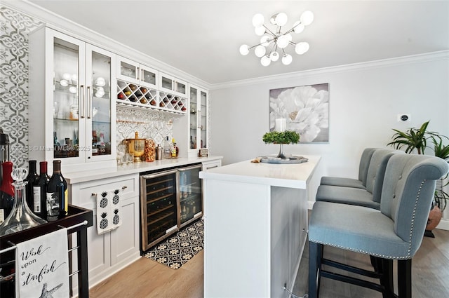 bar featuring white cabinets, crown molding, light hardwood / wood-style floors, beverage cooler, and a chandelier