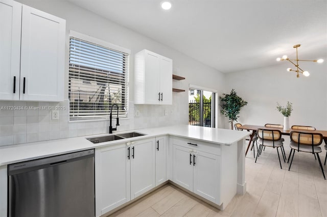 kitchen with kitchen peninsula, stainless steel dishwasher, sink, a chandelier, and white cabinetry