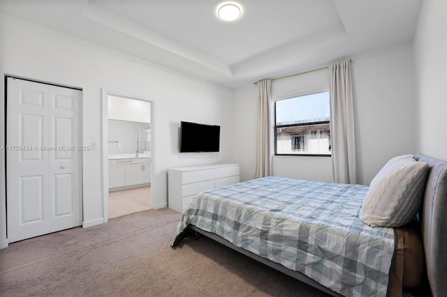 carpeted bedroom with ensuite bath and a tray ceiling