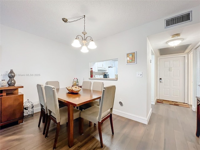 dining room with hardwood / wood-style floors, a textured ceiling, and an inviting chandelier