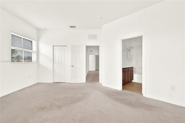 unfurnished bedroom featuring light carpet and ensuite bath