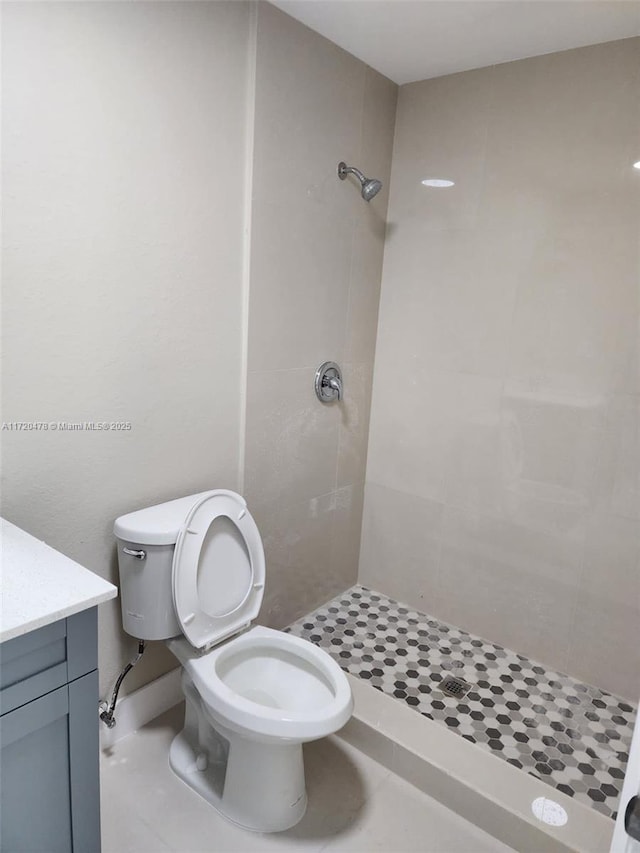 bathroom with tiled shower, tile patterned floors, vanity, and toilet