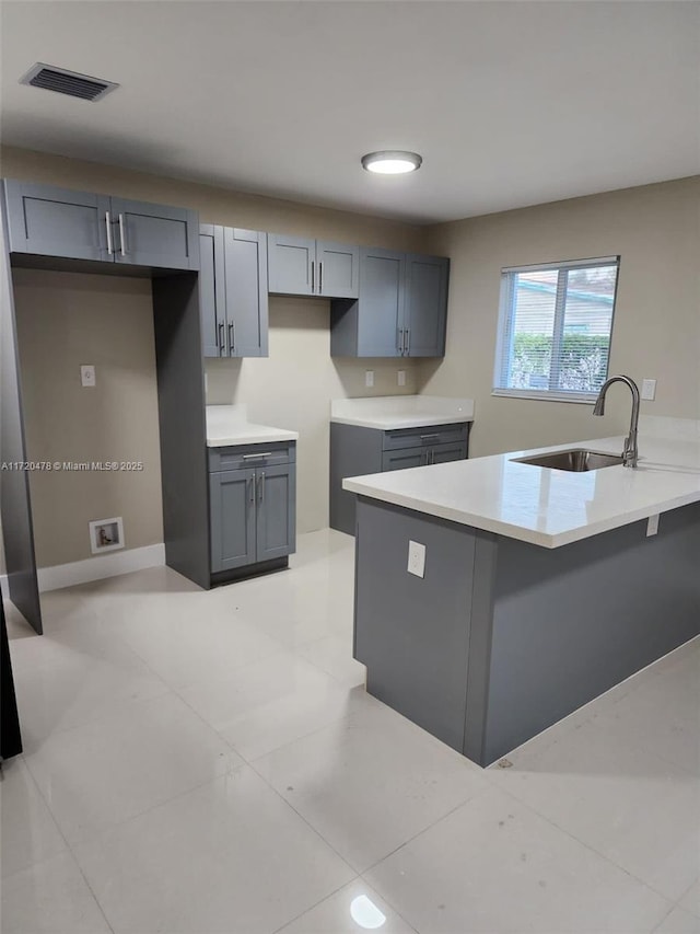 kitchen with gray cabinetry, kitchen peninsula, sink, and light tile patterned floors