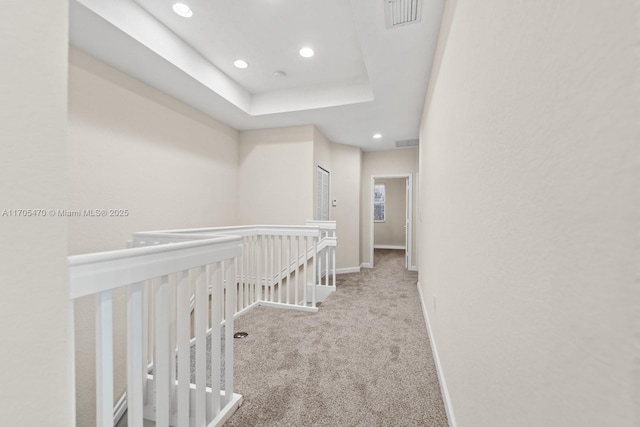 hall featuring a raised ceiling and light colored carpet