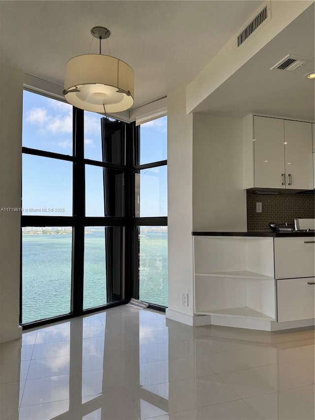 interior space with light tile patterned floors, a water view, plenty of natural light, and a wall of windows