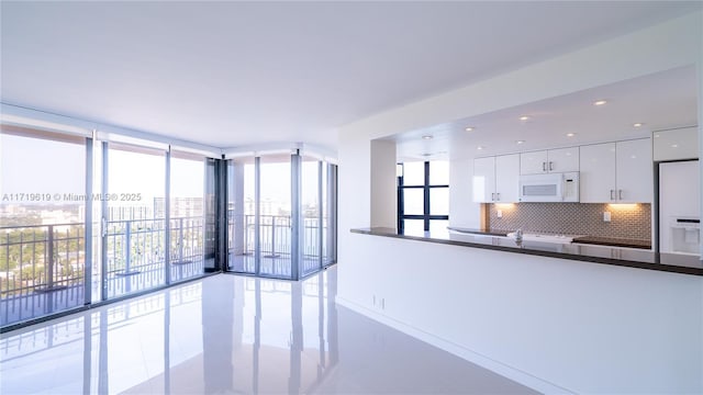 kitchen with white appliances, white cabinets, decorative backsplash, expansive windows, and dark countertops