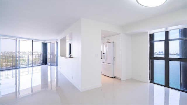 unfurnished room with light tile patterned floors, baseboards, and a wall of windows