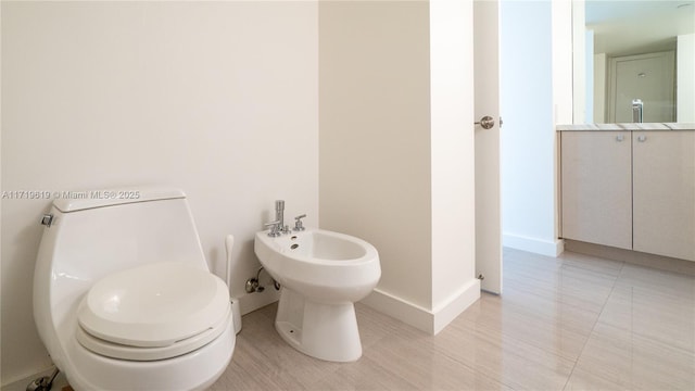 half bathroom with toilet, a bidet, vanity, and baseboards