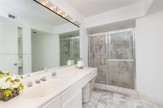 bathroom with a textured ceiling, vanity, and a shower with door