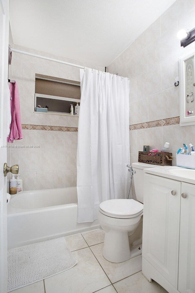 full bathroom with shower / bathtub combination with curtain, tile patterned floors, toilet, vanity, and tile walls