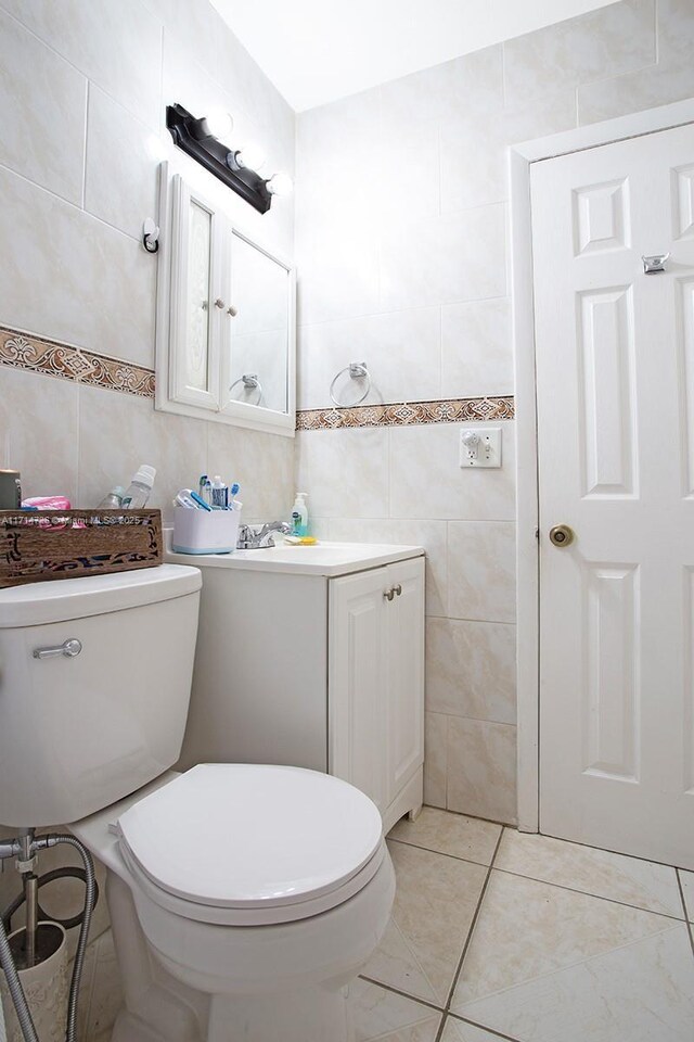 bathroom featuring tile patterned floors, vanity, toilet, and tile walls