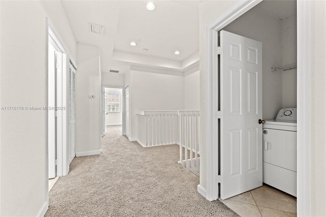 corridor with a raised ceiling, light carpet, and washer / clothes dryer