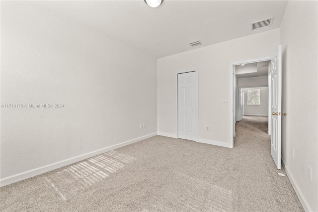 unfurnished bedroom with light colored carpet and a closet