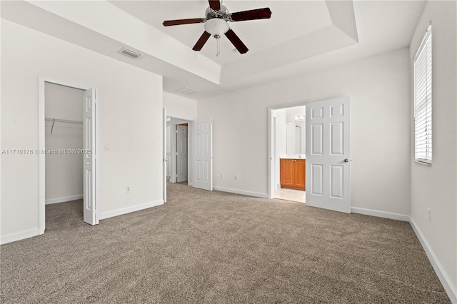 unfurnished bedroom featuring ceiling fan, a spacious closet, light colored carpet, a tray ceiling, and a closet