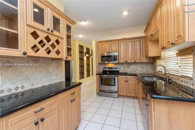 kitchen with sink, backsplash, dark stone counters, light tile patterned flooring, and appliances with stainless steel finishes