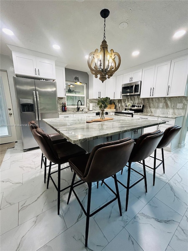 kitchen featuring appliances with stainless steel finishes, decorative light fixtures, white cabinetry, and a kitchen breakfast bar