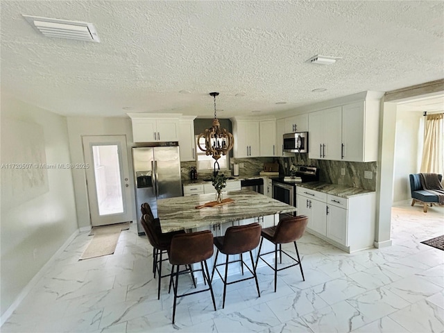 kitchen featuring white cabinetry, stainless steel appliances, tasteful backsplash, dark stone counters, and decorative light fixtures