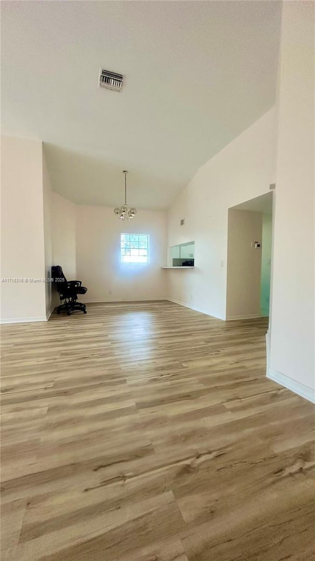 empty room featuring a chandelier, lofted ceiling, and light wood-type flooring